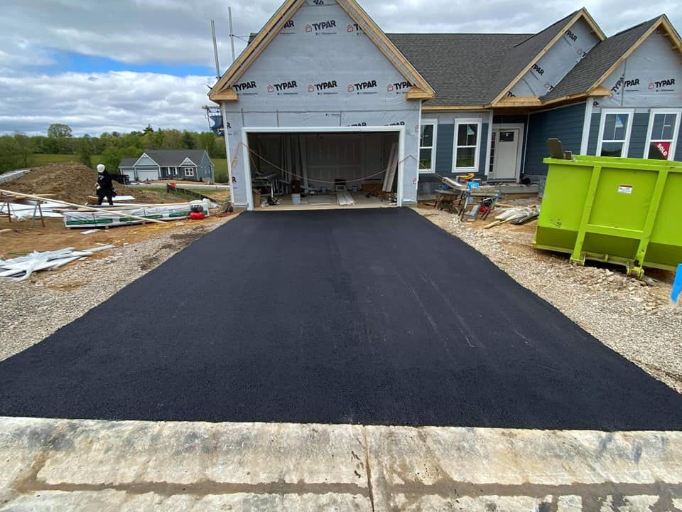New asphalt driveway leading to a house under construction; a green dumpster sits to the side.