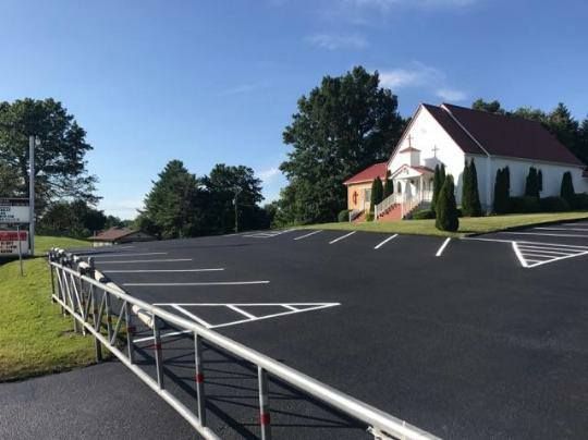 Paved parking lot in front of a white church with a red roof, under a blue sky.