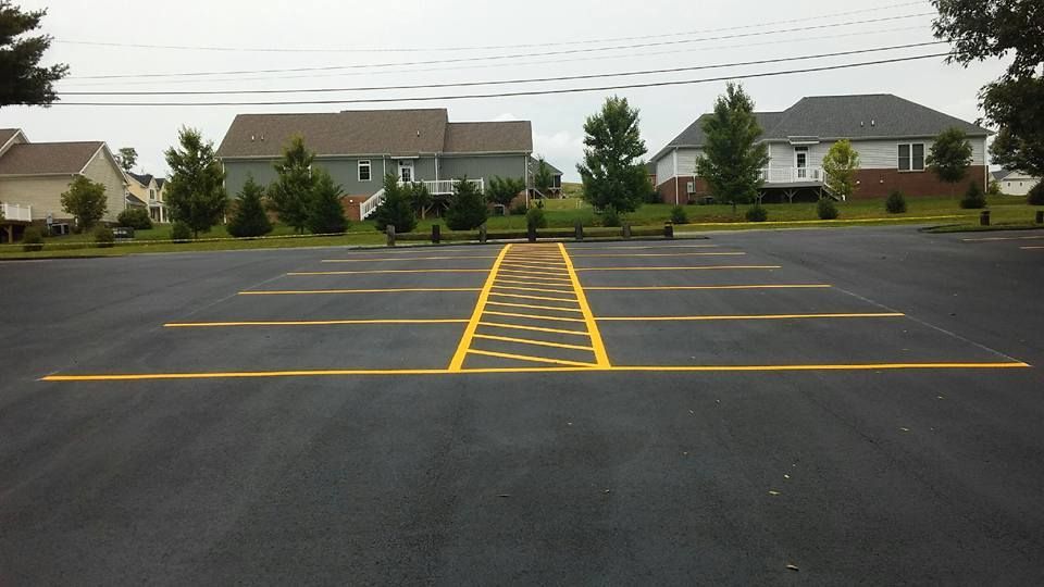 Asphalt parking lot with yellow painted lines and landscaping in the background.