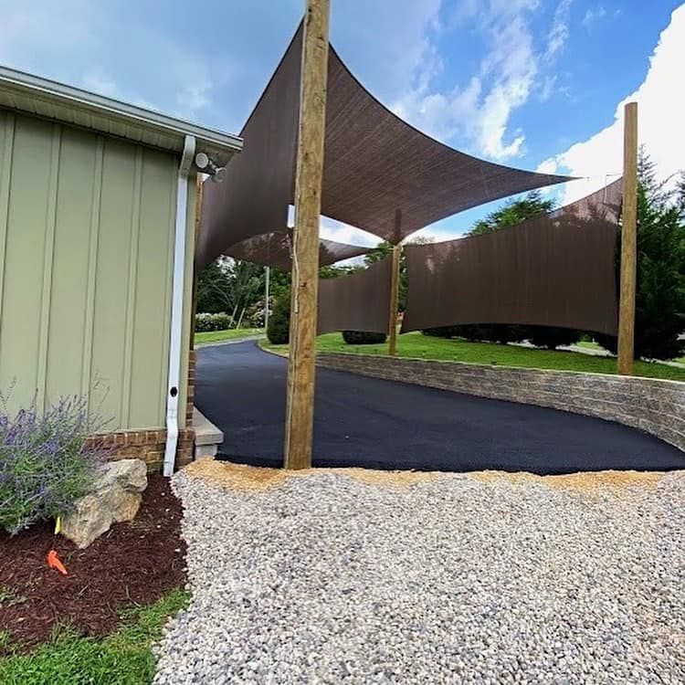 Driveway with shade sails supported by wooden posts. Brown sails and walls, asphalt and gravel.