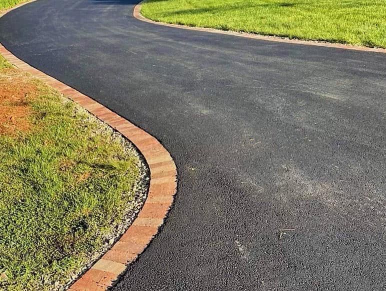 Asphalt driveway with brick border and grassy edge.