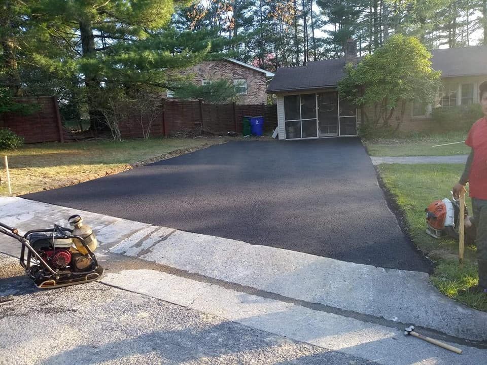 Newly paved asphalt driveway with a worker holding equipment.