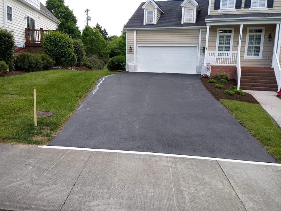 Asphalt driveway leading to a garage door, flanked by green grass and a house.
