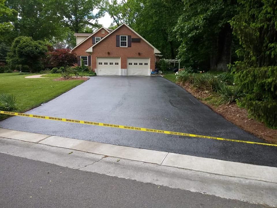 Newly paved asphalt driveway leading to a brick house with a two-car garage. Yellow caution tape across the driveway.