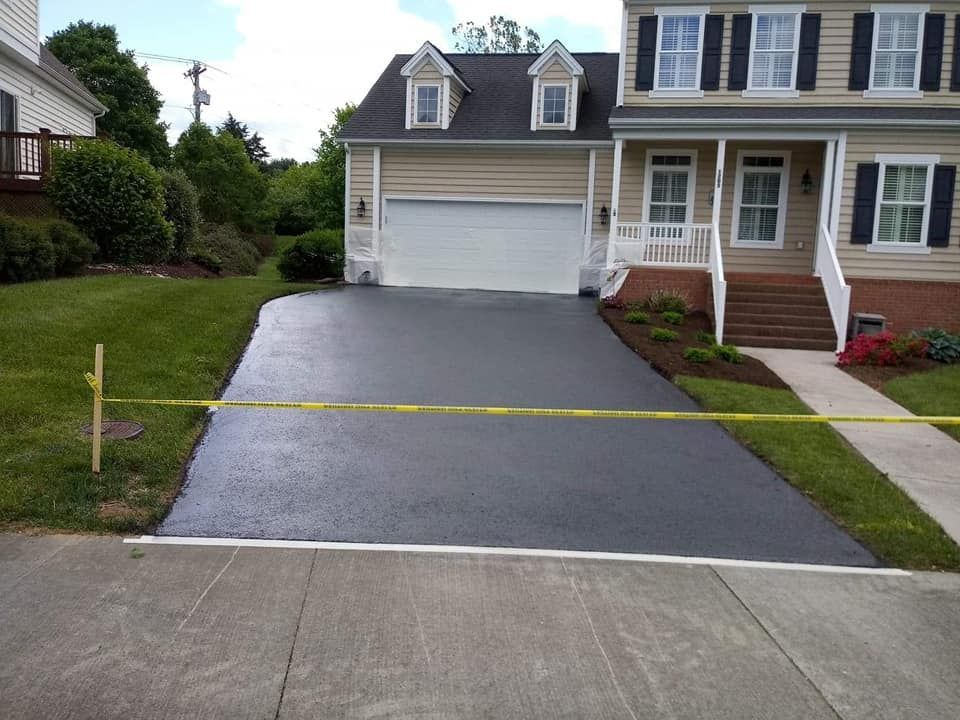 Newly paved asphalt driveway in front of a two-story beige house with a two-car garage.