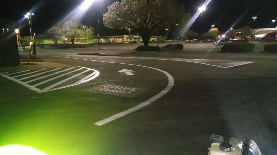 Night view of a parking lot with painted white directional arrows and markings. Streetlights illuminate the asphalt.