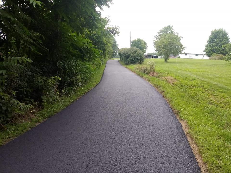 Paved path winds through green fields and trees on a cloudy day.