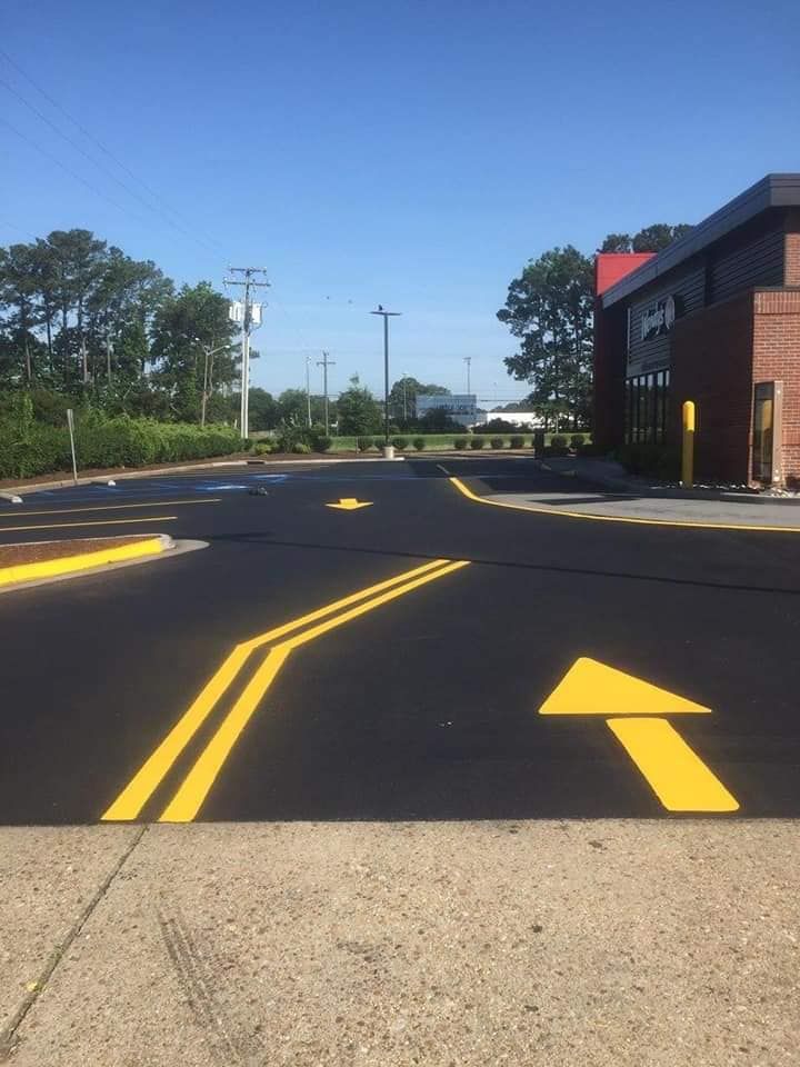 Yellow arrows and lines on black asphalt direct traffic in a parking lot. Building in background.