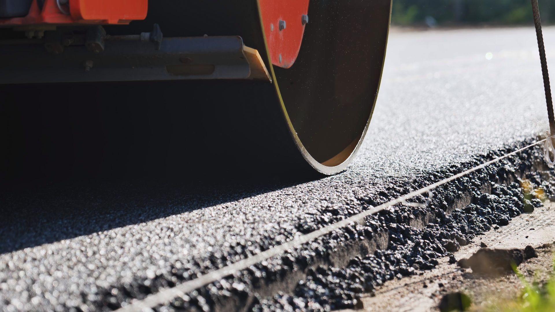 Road roller compacting fresh asphalt along a wet roadside