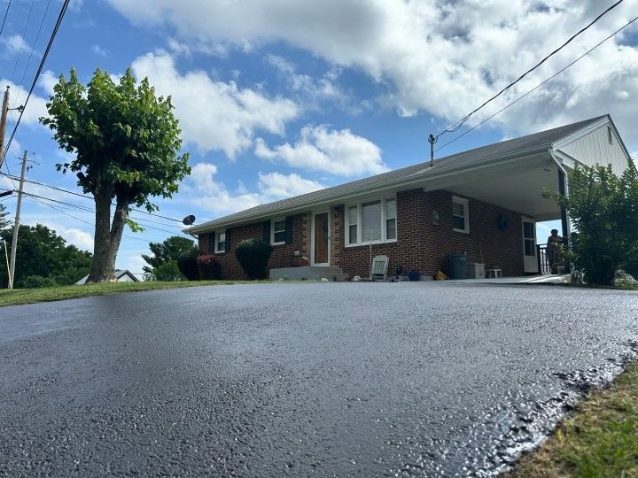 A brick house with a newly paved driveway under a cloudy sky.