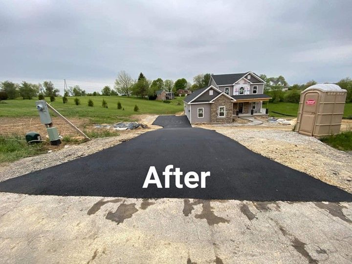 Newly paved asphalt driveway leading to a house under construction; a portable toilet is on the right.