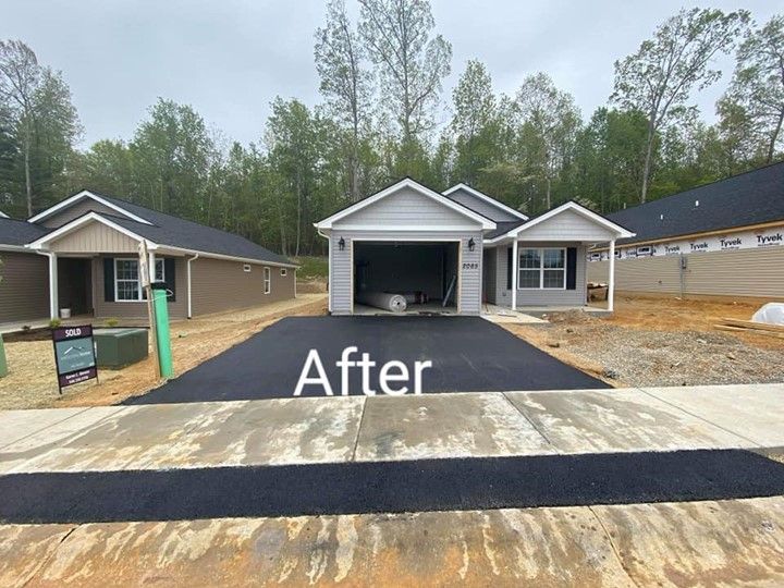 Newly paved driveway in front of a gray house with an open garage, trees in the background.