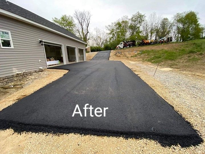 Newly paved asphalt driveway leading to a three-car garage. Construction equipment on the hill in the background.
