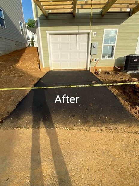 Newly paved asphalt driveway leading to a garage. Dirt and construction fencing surround the area.
