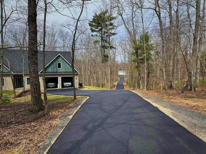 Asphalt driveway leading to a house with a two-car garage, surrounded by trees.