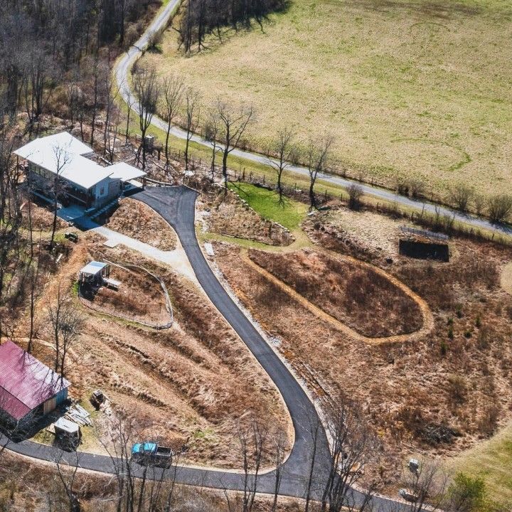 Aerial view of a home with a curved driveway, outbuildings, and surrounding fields.