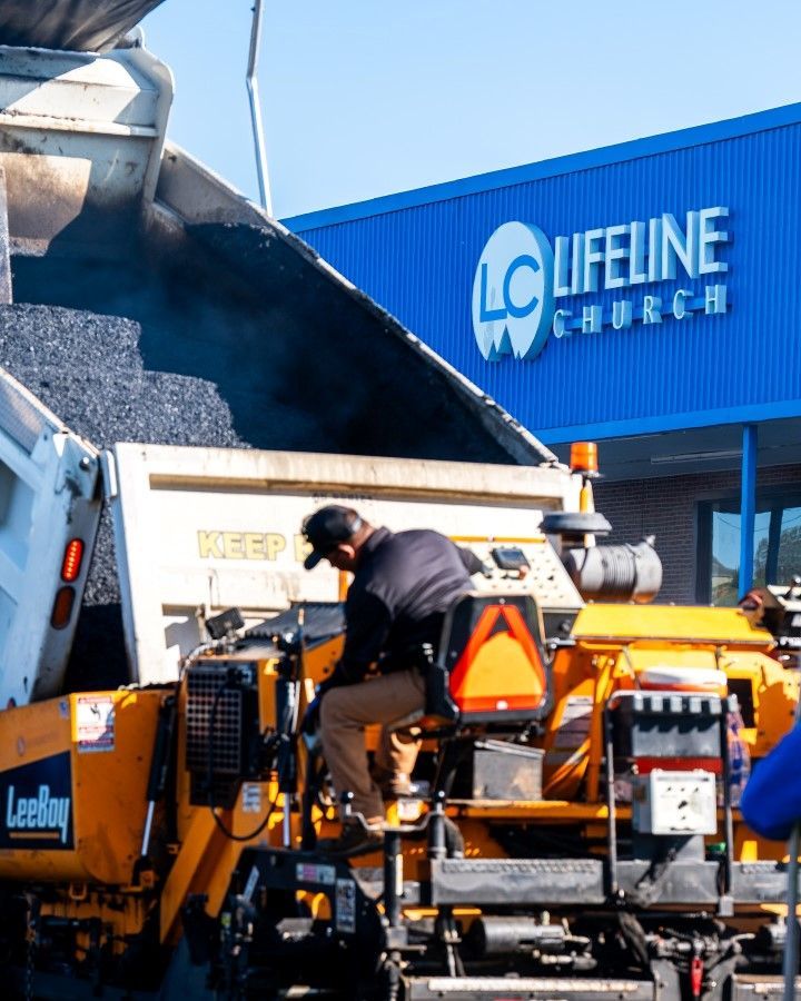 Asphalt paving in progress. A worker on an orange machine receives asphalt from a truck.