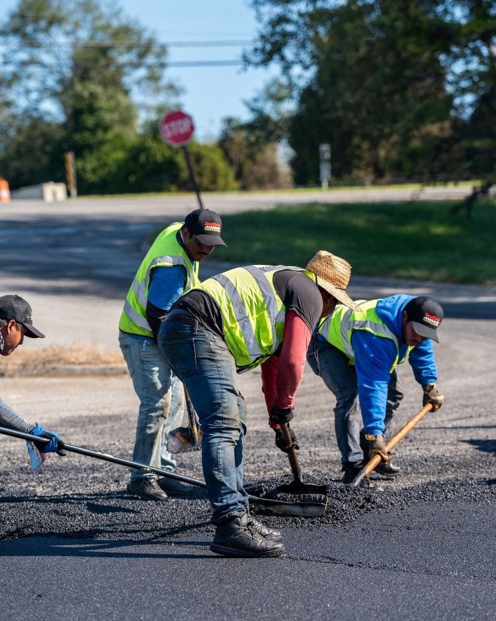 Road crew paving asphalt; wearing vests and hats, using tools on a street.