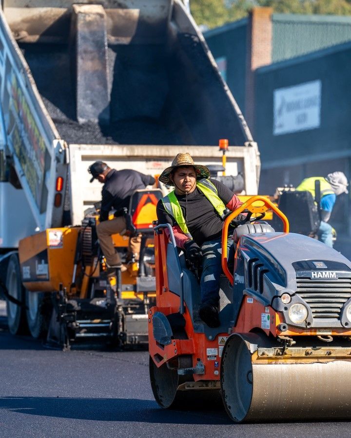 Road construction: workers paving street with machinery, including a roller and asphalt truck.