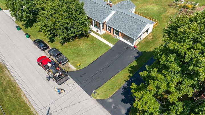 Aerial view of asphalt driveway being paved next to a house, with workers and vehicles present.