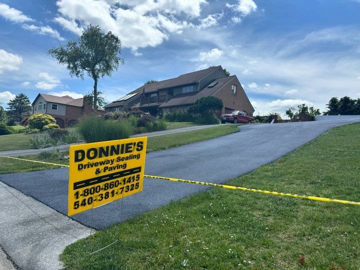 Sign for Donnie's Driveway Sealing & Paving in front of a house with a newly paved driveway.