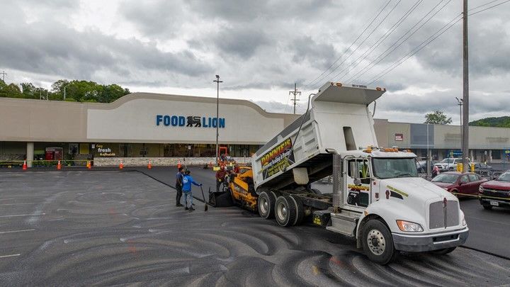 Asphalt paving in progress at Food Lion. A dump truck unloads asphalt for paving machine in parking lot.