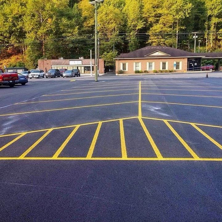 Yellow parking lines on black asphalt, cars parked nearby. Buildings and trees in the background.
