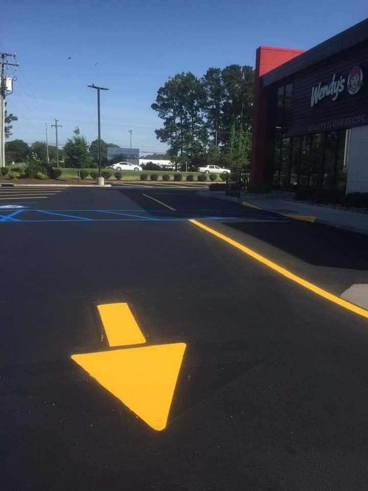 Yellow arrow on asphalt pavement, directing towards a Wendy's restaurant.