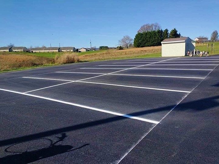 Freshly painted asphalt parking lot with white lines, blue sky, and a small building in the background.