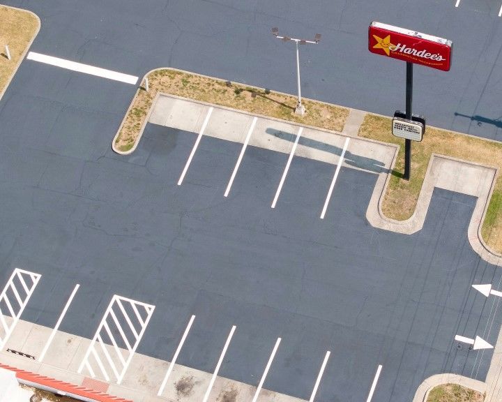 Asphalt parking lot with white parking space lines. A Hardee's sign is visible.