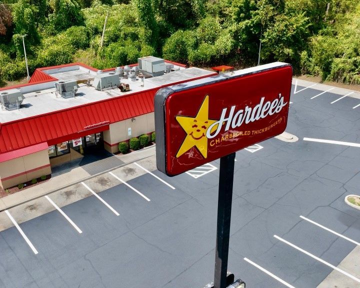 Hardee's restaurant sign and building with empty parking lot. Red sign, red roof, tan building, green trees.