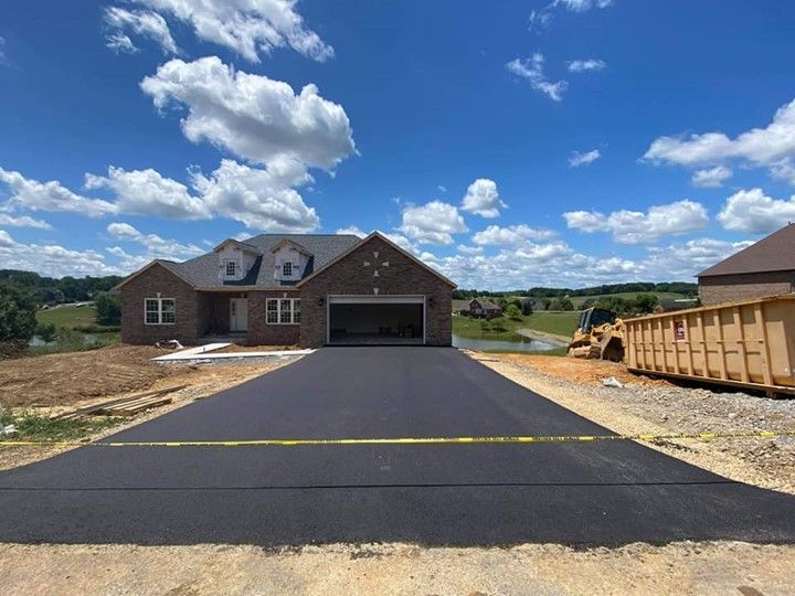 New home with asphalt driveway; brown brick exterior, open garage, blue sky, and construction container.