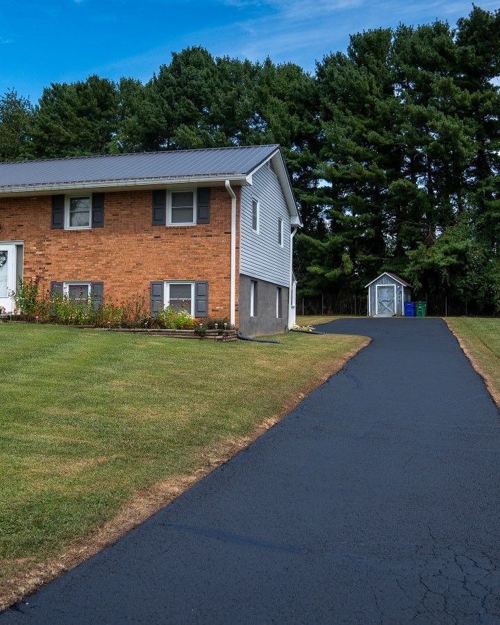 Two-story house with brick and siding, black asphalt driveway, and shed under a blue sky.