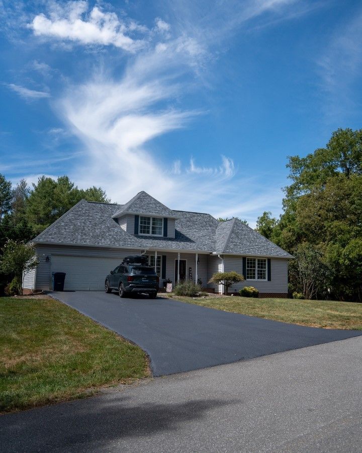 Suburban home with a black car in the driveway, blue sky with wispy clouds overhead.
