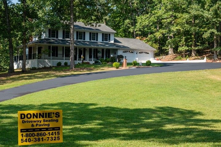 Two-story house with long driveway and sign for Donnie's Driveway Sealing & Paving in a green yard.
