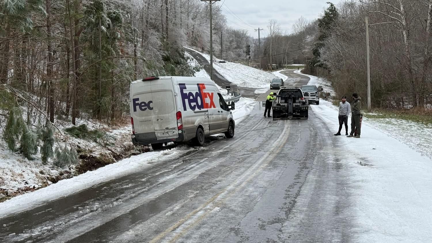 FedEx van and workers on a snowy, icy roadside after a winter slide-off.