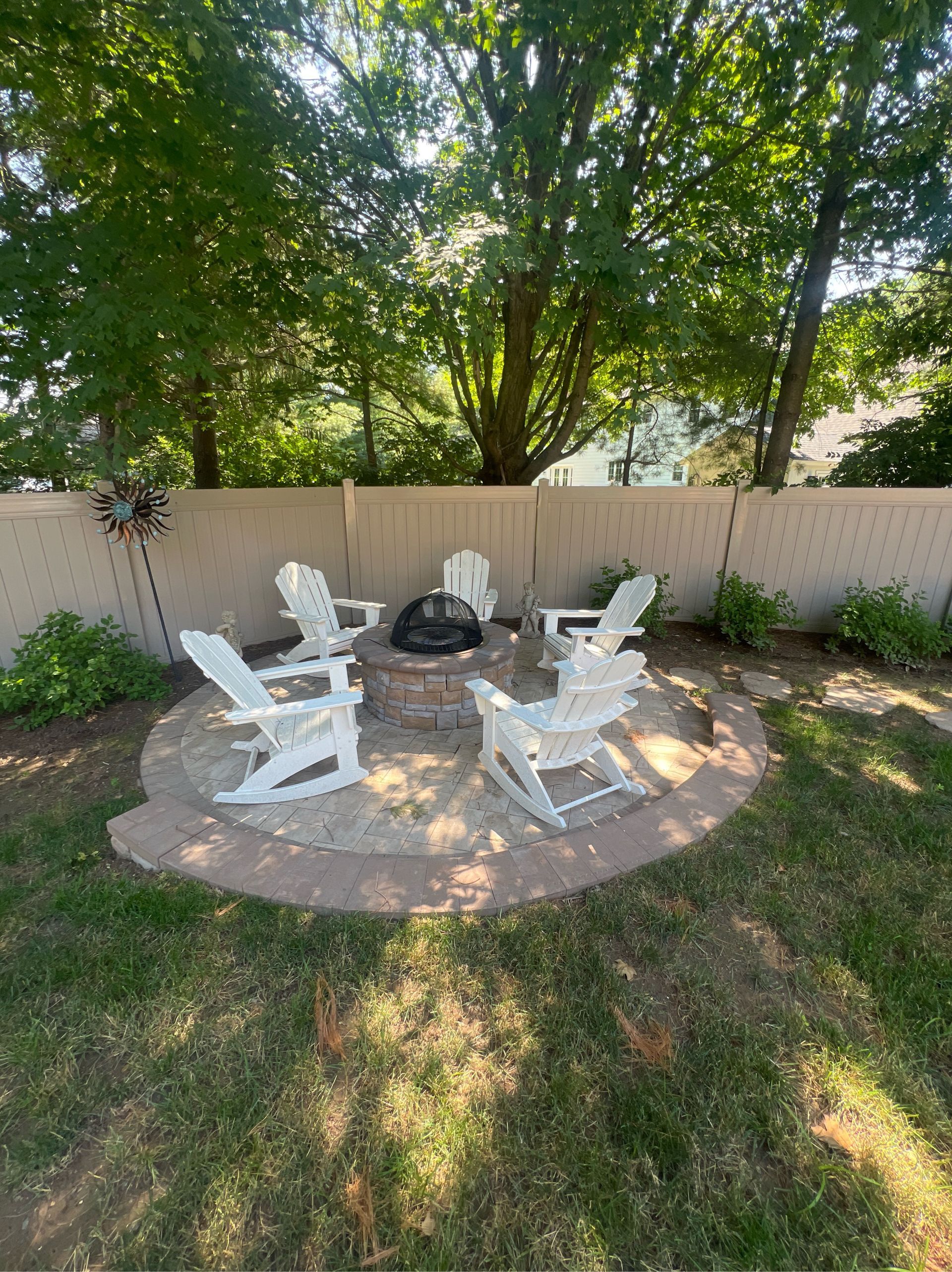 Fire pit area with six white Adirondack chairs, in a backyard.