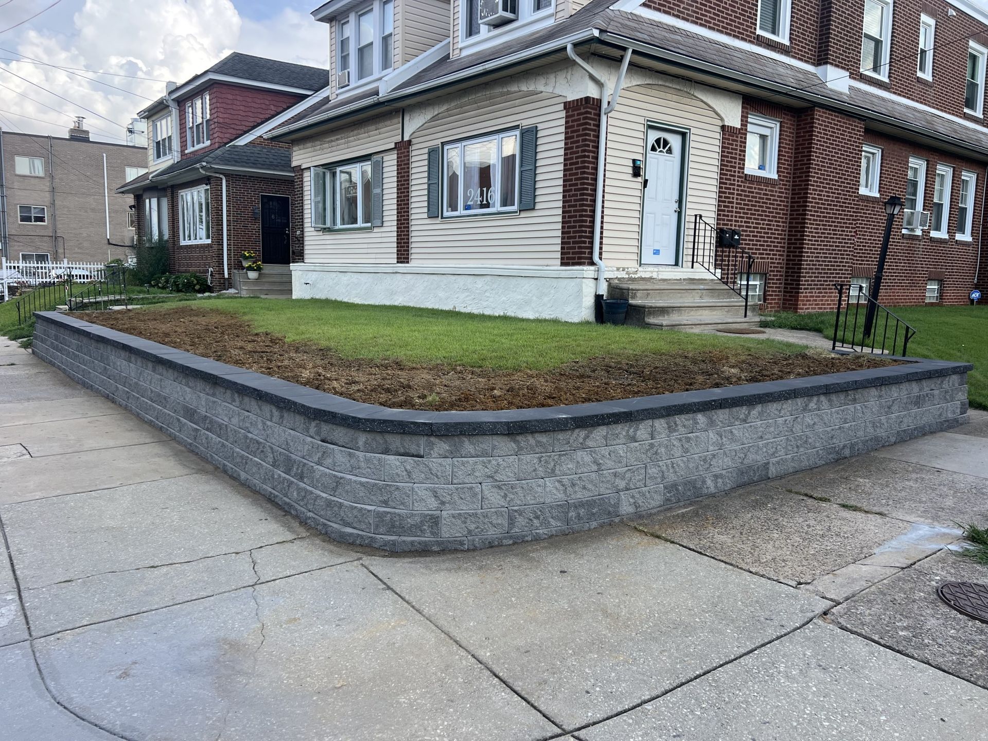 Brick home with gray retaining wall, green grass, and sidewalk.