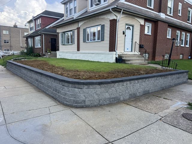 Brick home with gray retaining wall, green grass, and sidewalk.