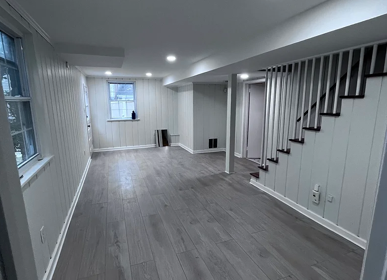 Empty basement room with gray flooring, white walls, and a staircase along the right side.