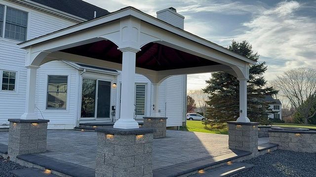 Patio with a white covered structure, pillars, and a brick base.