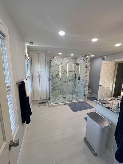 Spacious bathroom with glass shower, white cabinets, and light gray walls. Bright and modern design.