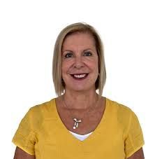 Woman with short blonde hair wearing a yellow shirt smiling at the camera.
