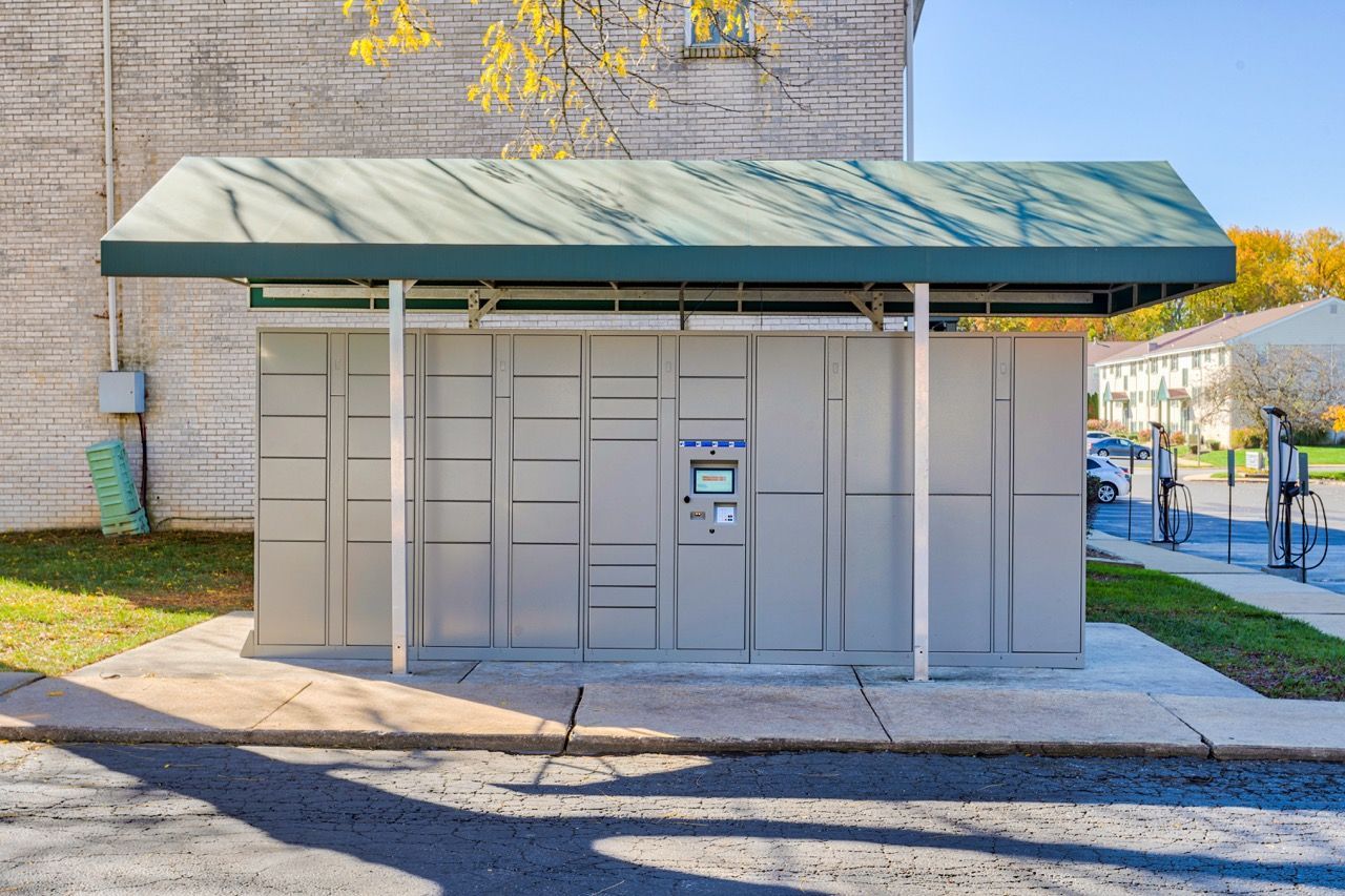 Brookbend Apartments Outdoor parcel lockers with a control kiosk, located along the building exterior for resident package pickup.