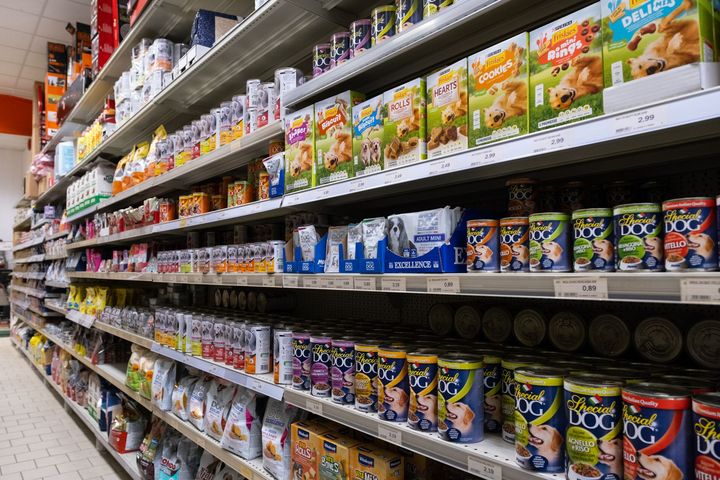 Corridoio degli scaffali di un supermercato pieno di scatole e lattine di cibo per animali di vario tipo e colore.
