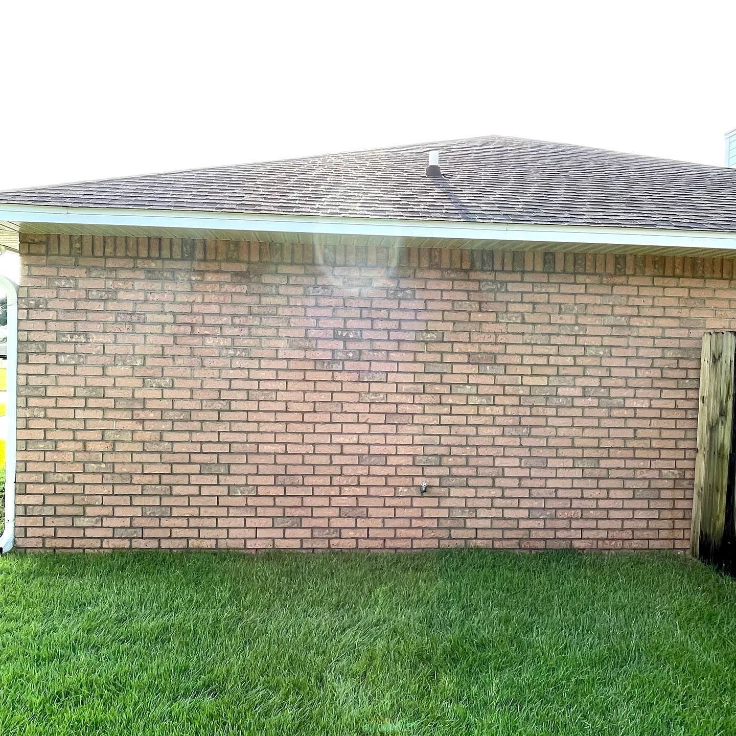 Brick wall of a building with a shingled roof, next to green grass and a wooden post.