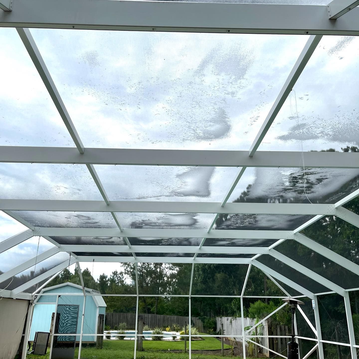 White-framed screened-in porch with a cloudy sky view. A small blue shed is visible in the backyard.