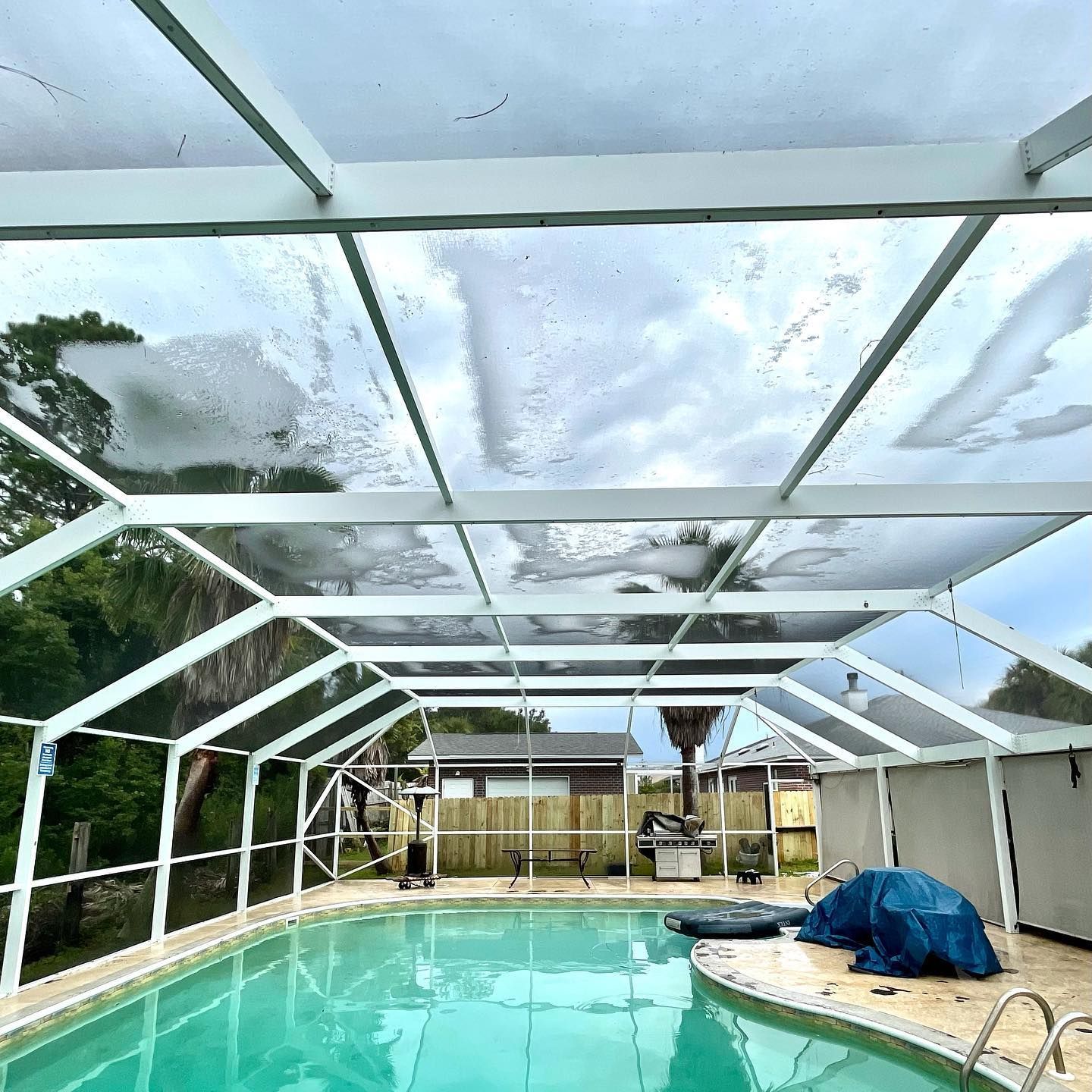 Pool under a white-framed enclosure with a clear roof, on a cloudy day.