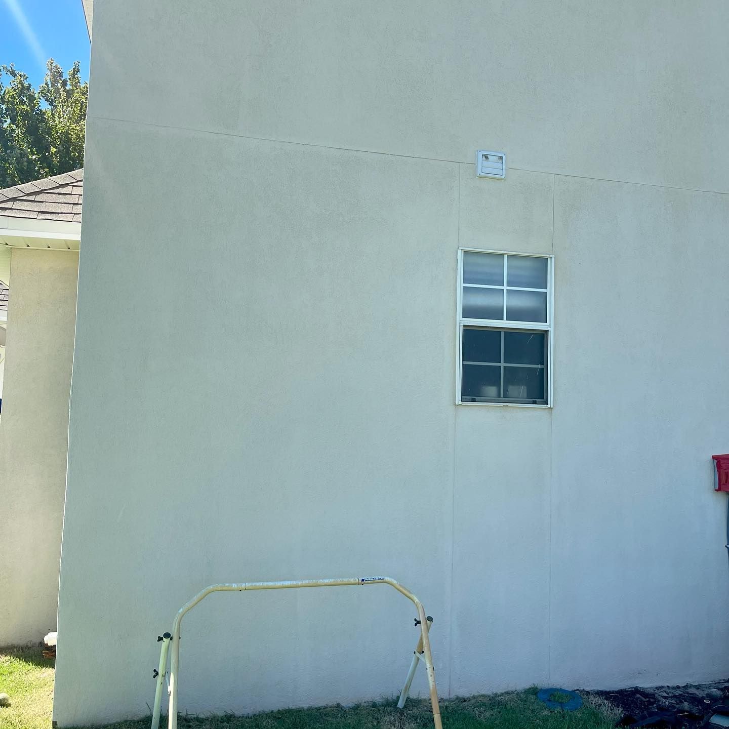 Exterior wall of a light-colored building with a window and a small frame-like object in front.