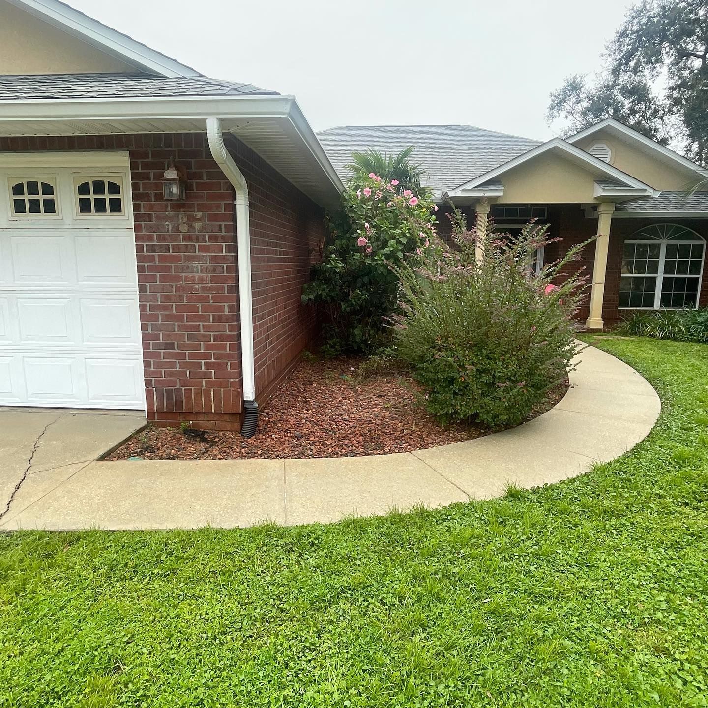 A house with a white garage door, brick wall, and a curved sidewalk in front of green grass.